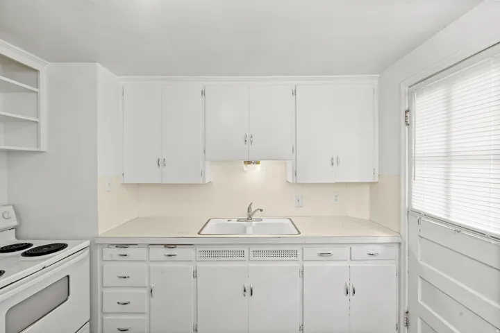 White cabinetry, white countertop, double basin sink, built-in shelving, and a window with blinds