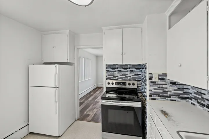 Kitchen featuring white cabinetry, a mosaic tile backsplash, white appliances, and wood-finish flooring visible in the adjacent room