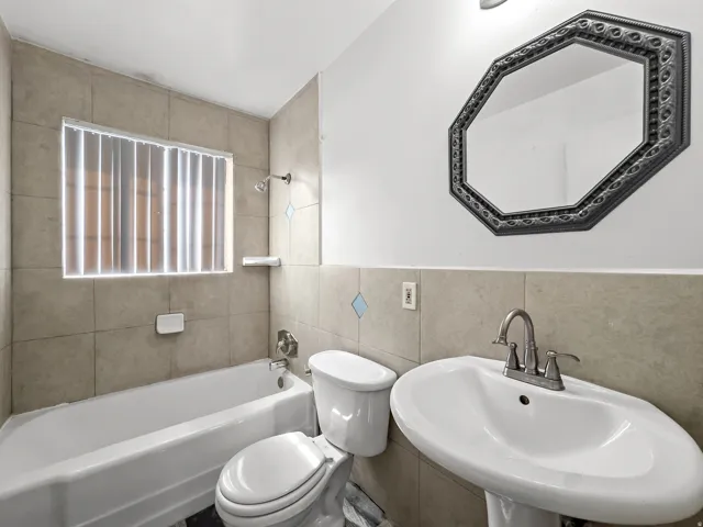 Pedestal sink with a chrome faucet, octagon-shaped decorative mirror, ceramic tile half-wall, tiled shower surround, and a white bathtub