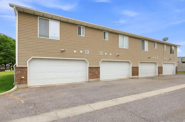 Multiple attached garages with white panel doors, beige siding exterior, and brick detailing