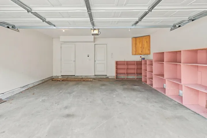 Spacious garage with concrete flooring, panel garage door, built-in shelving, and light wood-tone cabinetry