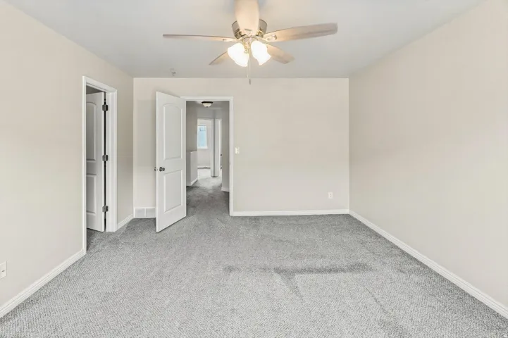 Neutral wall tones, gray carpeting, white trim, paneled doors, and a ceiling fan with integrated lighting
