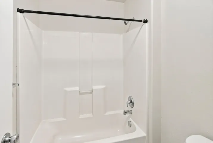 Bathtub with an integrated shower surround, chrome shower fixtures, and a black shower rod