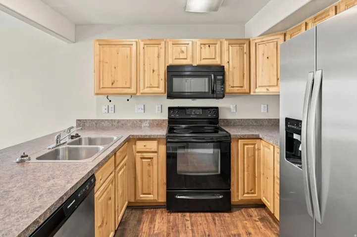 U-shaped kitchen with wood-finish cabinetry, stainless steel refrigerator, black range, and dual basin sink