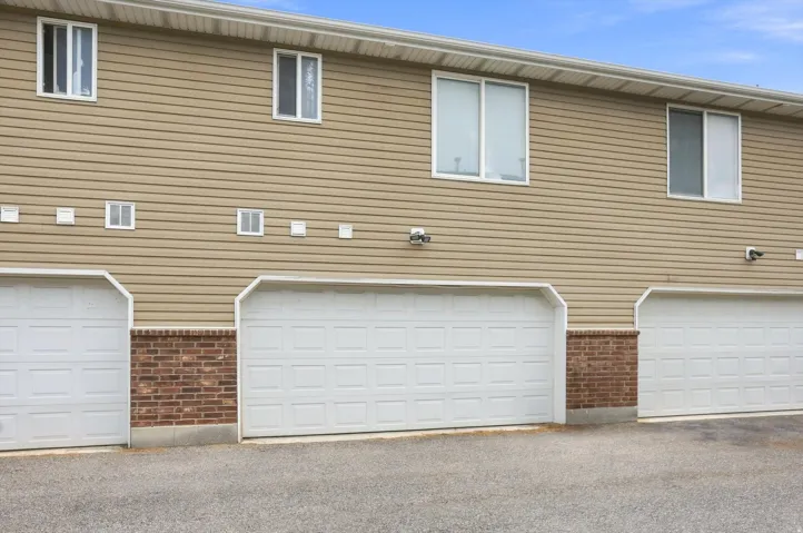 Tan horizontal siding exterior with multiple white-framed windows, individual garage doors, and brick accents