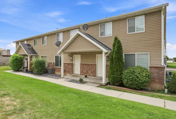 Two-story exterior with vinyl siding and brick accents, individual covered entryways, mature landscaping, and an expansive lawn