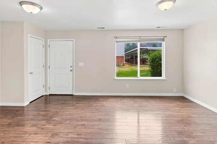 Wood-finish flooring, neutral wall tones, window with roller shade, two ceiling-mounted light fixtures, and white trim throughout
