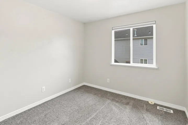 Neutral wall paint, gray carpet flooring, and a single window with white trim