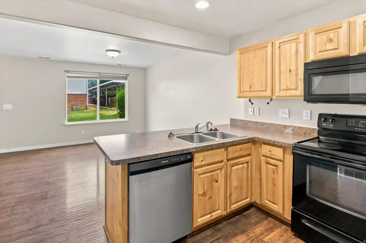 Kitchen featuring wood-finish cabinetry, a black oven range, black microwave, and a stainless steel dishwasher