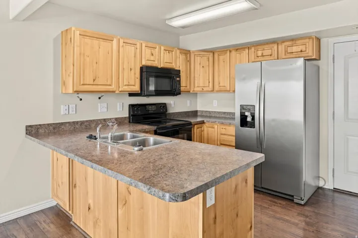 Kitchen featuring wood cabinetry, a double basin sink, stainless steel refrigerator, black range, and wood-finish flooring