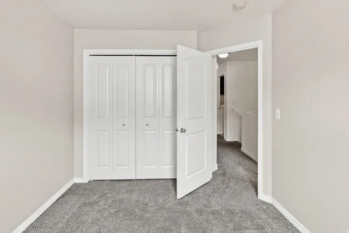Neutral-toned walls, gray carpeting, white bi-fold closet doors, and white interior door