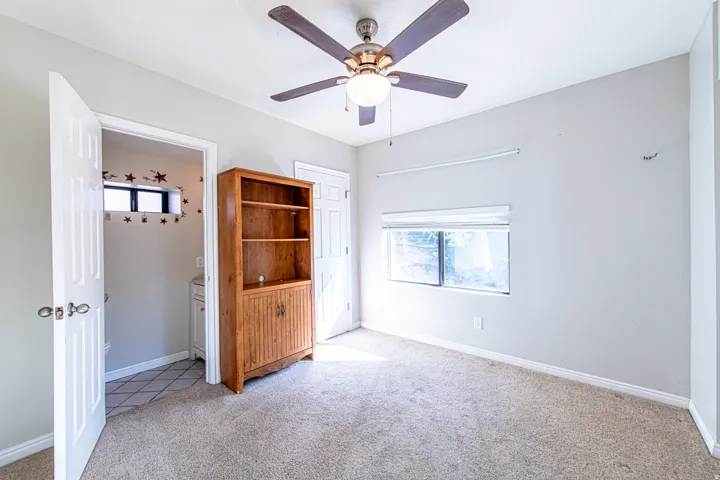 Wall-to-wall carpeting, window with roller shade, and ceiling fan with integrated lighting
