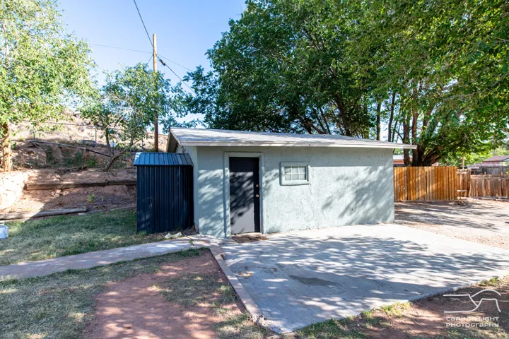 Detached utility building with a textured stucco finish, composition shingle roof, and a privacy fence