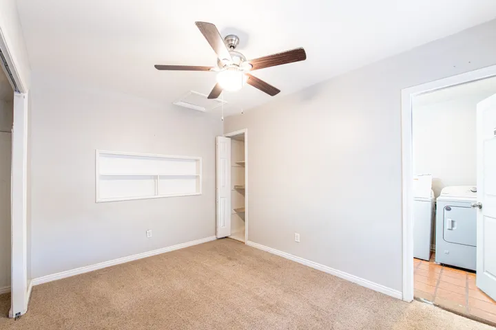 Ceiling fan with light fixture, built-in shelving, carpet flooring, and an adjacent laundry area with tile flooring
