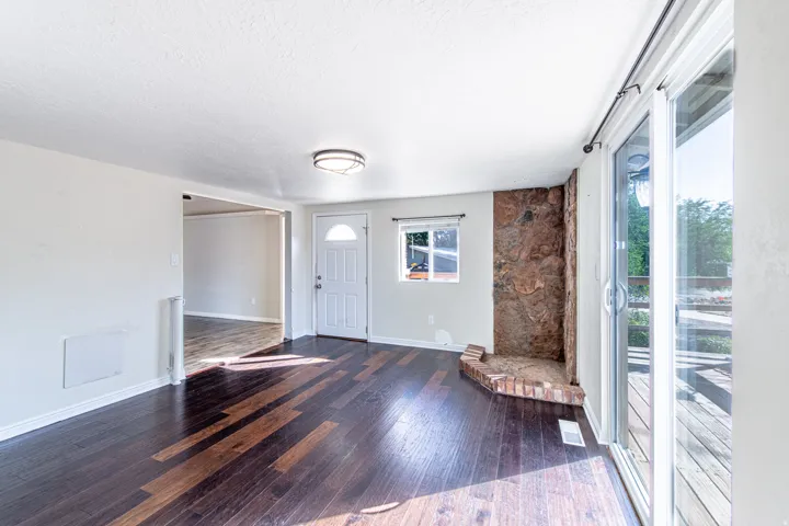 Dark wood-finish flooring, stone accent wall, sliding glass patio doors, window with white blinds, and a white paneled entry door