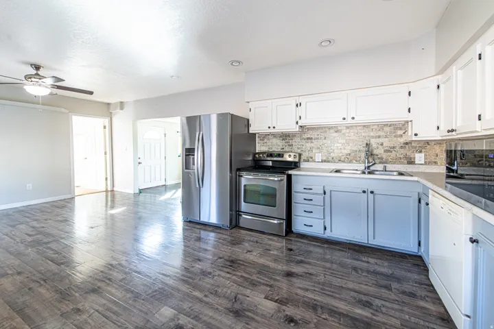 Kitchen featuring stainless steel appliances, upper white cabinetry, lower blue cabinetry, mosaic tile backsplash, and wood-finish flooring
