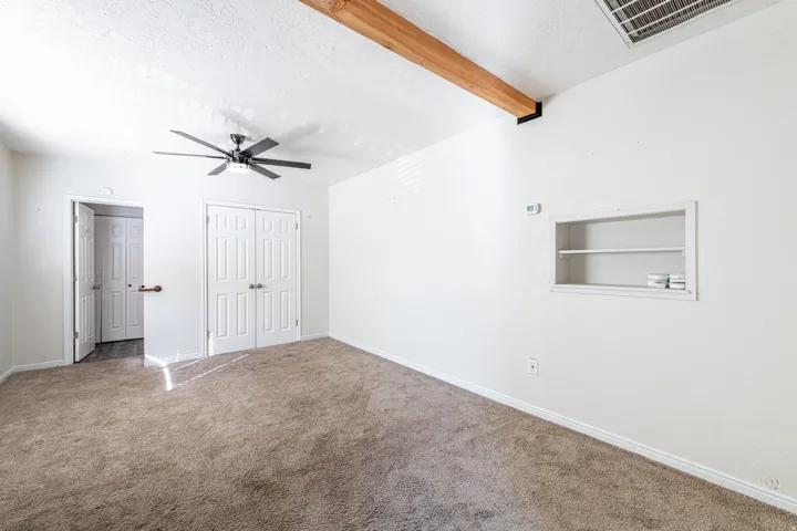 Tray ceiling with exposed wood beam, ceiling fan, built-in shelving, carpet flooring, and white paneled doors