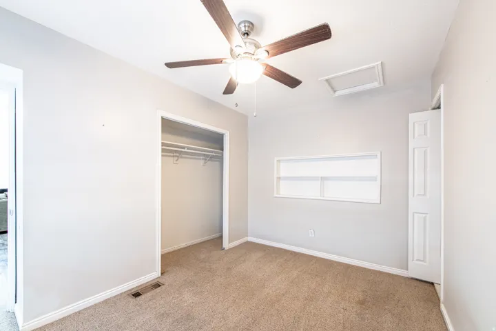 Carpeted room featuring a ceiling fan with light, built-in shelving, and a bi-fold closet
