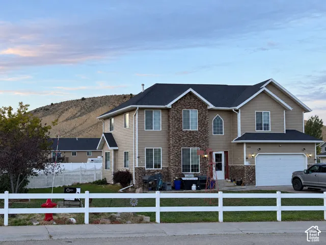 Two-story residence with a two-car garage, stone and siding exterior, and a white picket fence