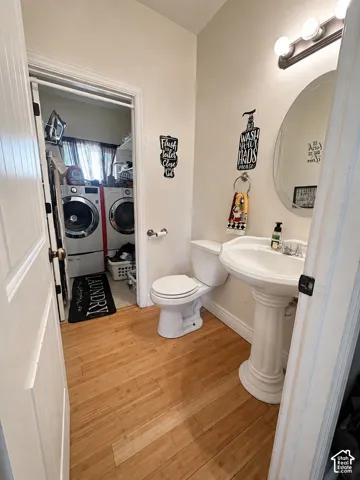 Pedestal sink with an oval mirror, three-light vanity fixture, and wood-finish flooring