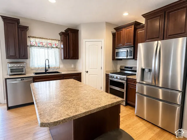 Kitchen featuring dark wood cabinetry, stainless steel appliances, a center island with a light-colored countertop, and light wood-finish flooring