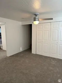 Textured carpeting, white walls, ceiling fan with integrated lighting, and panel-style closet doors