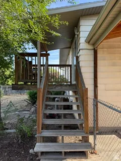 Raised wooden deck and staircase with wood railing, featuring a chain-link fence