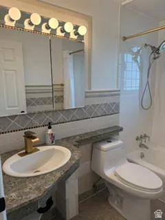 Bathroom featuring a vanity with an undermount sink, a gold-tone faucet, a mirror with multi-bulb lighting, and a tiled shower-bathtub combination
