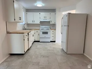 Kitchen featuring white cabinetry, wood-finish countertops, tile flooring, and white appliances