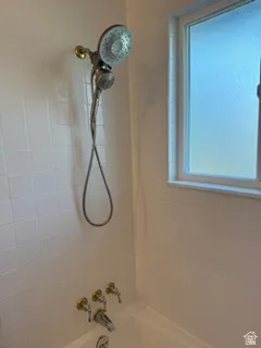 White tile surround with a tub and shower combination, featuring a handheld showerhead and a frosted window