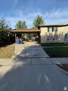 Brick and siding exterior with a covered carport, concrete driveway, and established trees