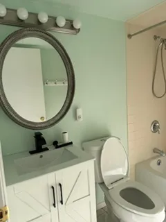 Vanity with an integrated sink and matte black faucet, framed mirror with overhead lighting, and a white toilet