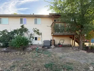 Exterior siding with multiple windows, featuring a wooden deck with railing and stairs, and mature trees