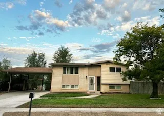 Split-level residence featuring a carport, brick and siding exterior, front lawn, and mature trees