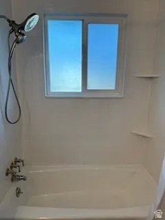 White tub with polished chrome and brass fixtures, a double shower head, and built-in corner shelving