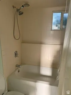 Built-in bathtub with a wall-mounted showerhead and separate handheld sprayer, surrounded by tiled walls
