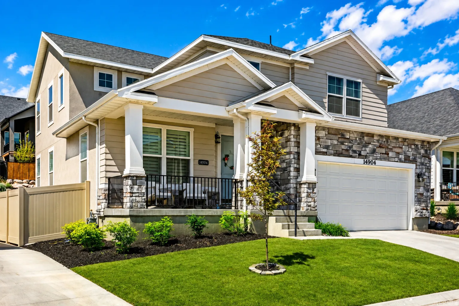 Two-story residence featuring a covered front porch, stone and siding exterior, two-car garage, and established landscaping