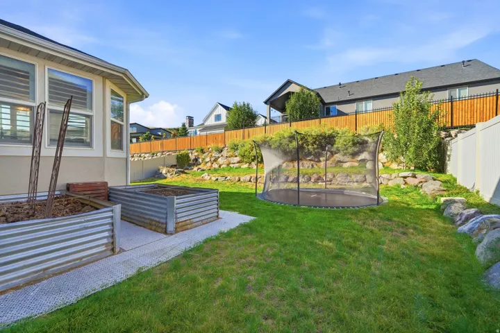 Expansive backyard featuring a manicured lawn, tiered landscaping with natural rock elements, and raised garden beds