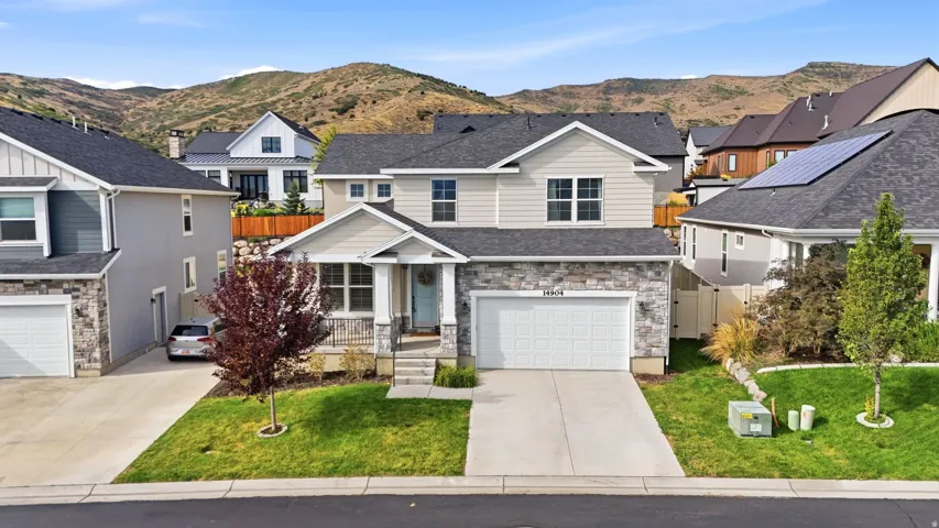 Charming two-story residence featuring a stone and siding exterior, two-car garage, covered front porch entry, and manicured front lawn with newly planted landscaping