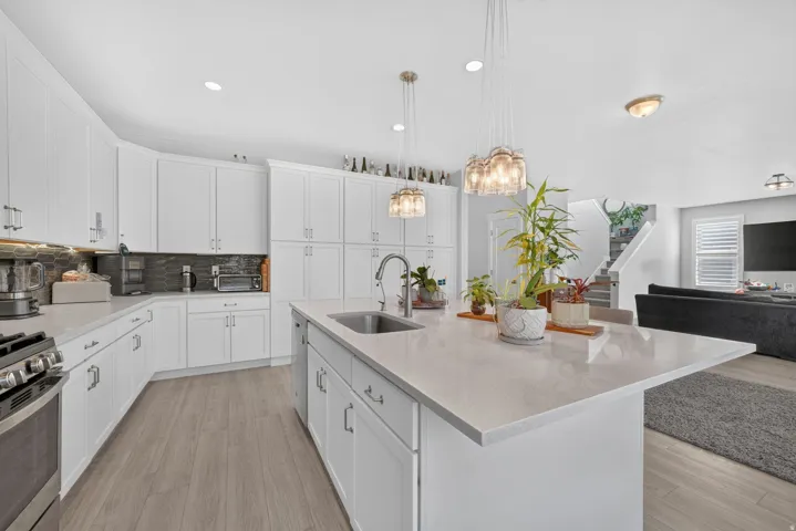 White shaker cabinetry, light-toned wood-finish flooring, recessed lighting, and a kitchen island with pendant lighting