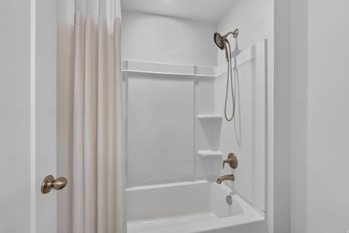 Tub and shower combination featuring a bronze-finish shower head, bronze-finish faucet, and integrated shelving