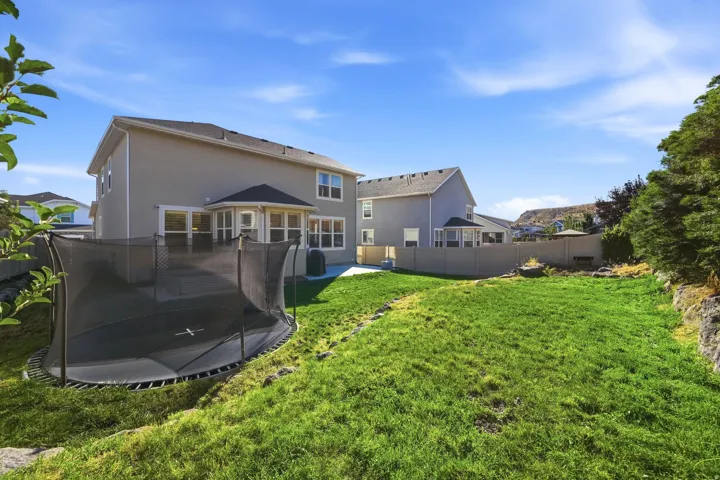 Expansive backyard featuring a green lawn, stucco exterior, and a sunroom with large windows