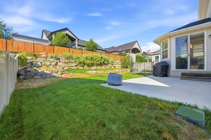 Expansive backyard featuring a manicured lawn, concrete patio, a rock retaining wall, and a wood privacy fence