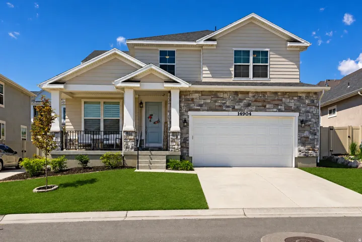 Stone veneer and horizontal siding exterior, covered porch with columns, attached two-car garage, concrete driveway, and manicured lawn