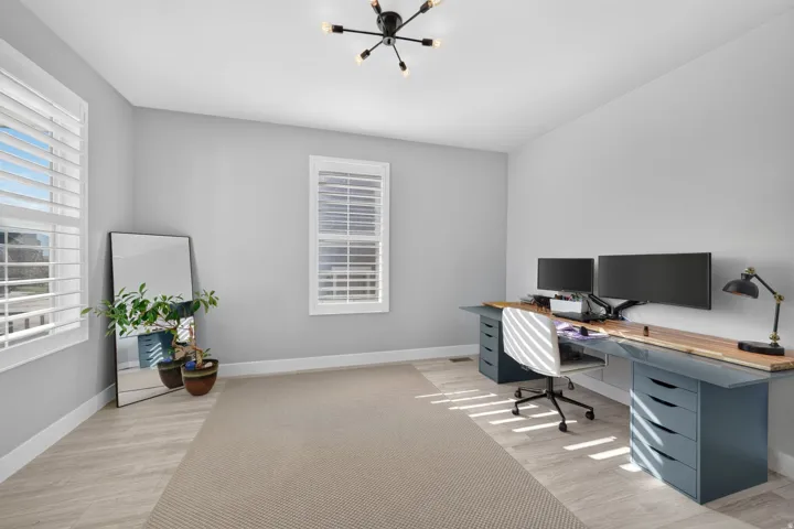 Hardwood-finish flooring with an area rug, dual windows featuring white plantation shutters, and a modern sputnik chandelier