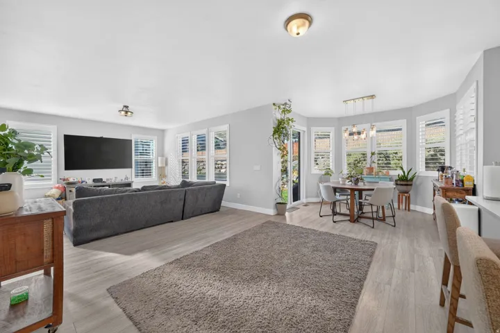 Expansive living area featuring light wood-finish flooring, multiple windows with white plantation shutters, and recessed lighting