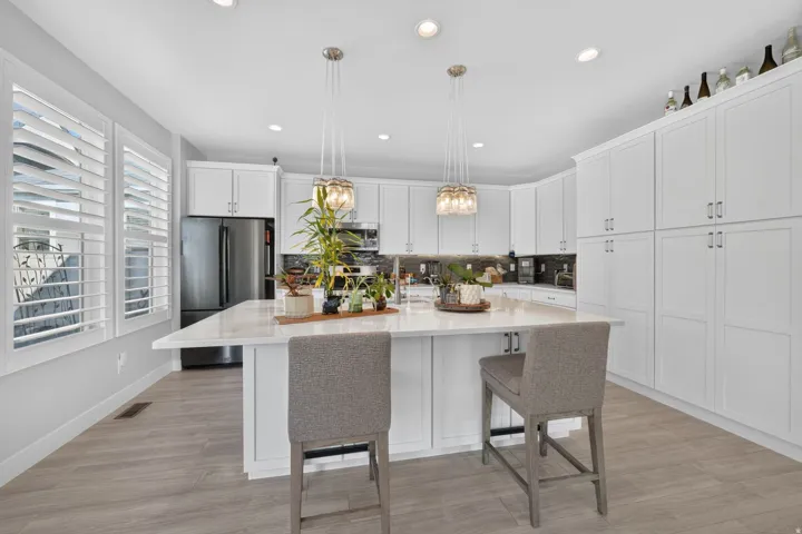 Spacious kitchen featuring an expansive center island, white cabinetry, stainless steel appliances, pendant lighting, and wood-finish flooring