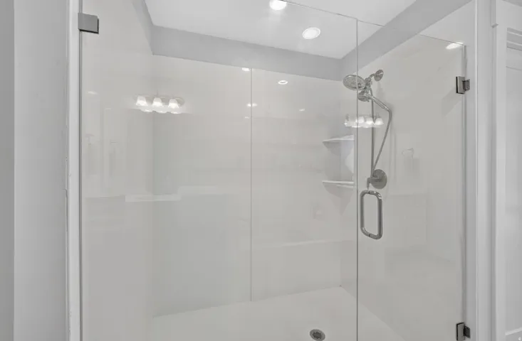Glass-enclosed shower with white paneling, integrated shelving, and a chrome shower fixture