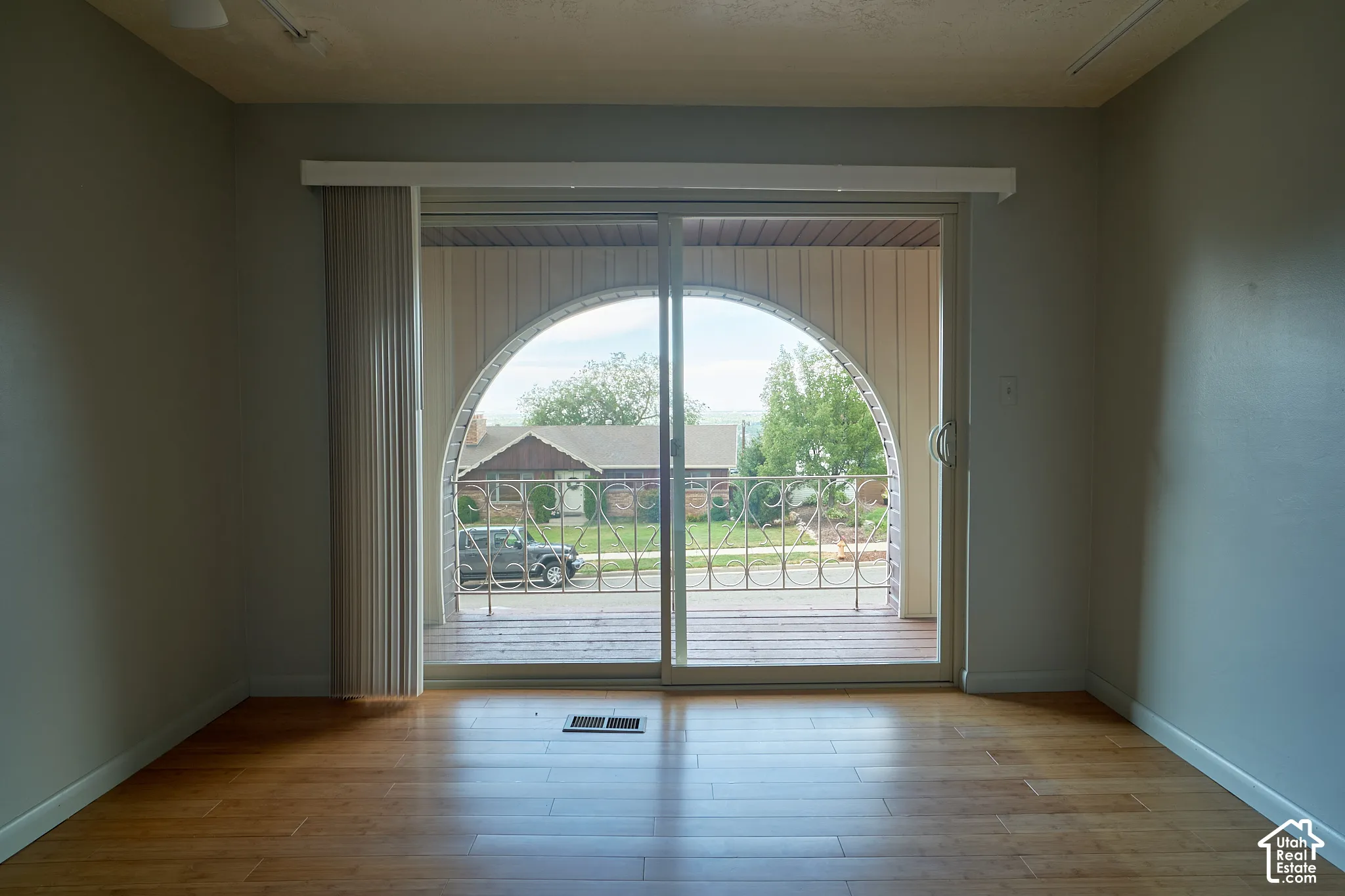 Sliding glass door leading to a balcony with an arched opening, wood-finish flooring, and light gray walls