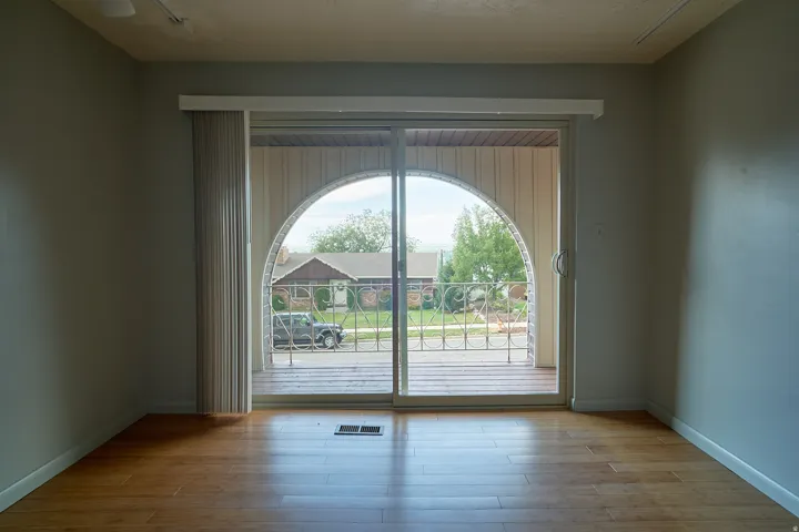 Sliding glass door leading to a balcony with an arched opening, wood-finish flooring, and light gray walls